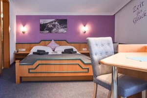 Habitación de hotel con una cama, una silla, una mesa y una pared con un cuadro y dos apliques.