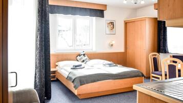 A bedroom with a bed, a desk, a chair, a wardrobe, and a window with curtains.