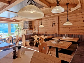 Un interior de madera con mesas y bancos, una chimenea de piedra y lámparas colgantes.