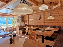Un interior de madera con mesas y bancos, una chimenea de piedra y lámparas colgantes.