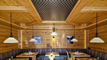 A wooden interior with high ceilings, patterned benches, and tables with chairs.