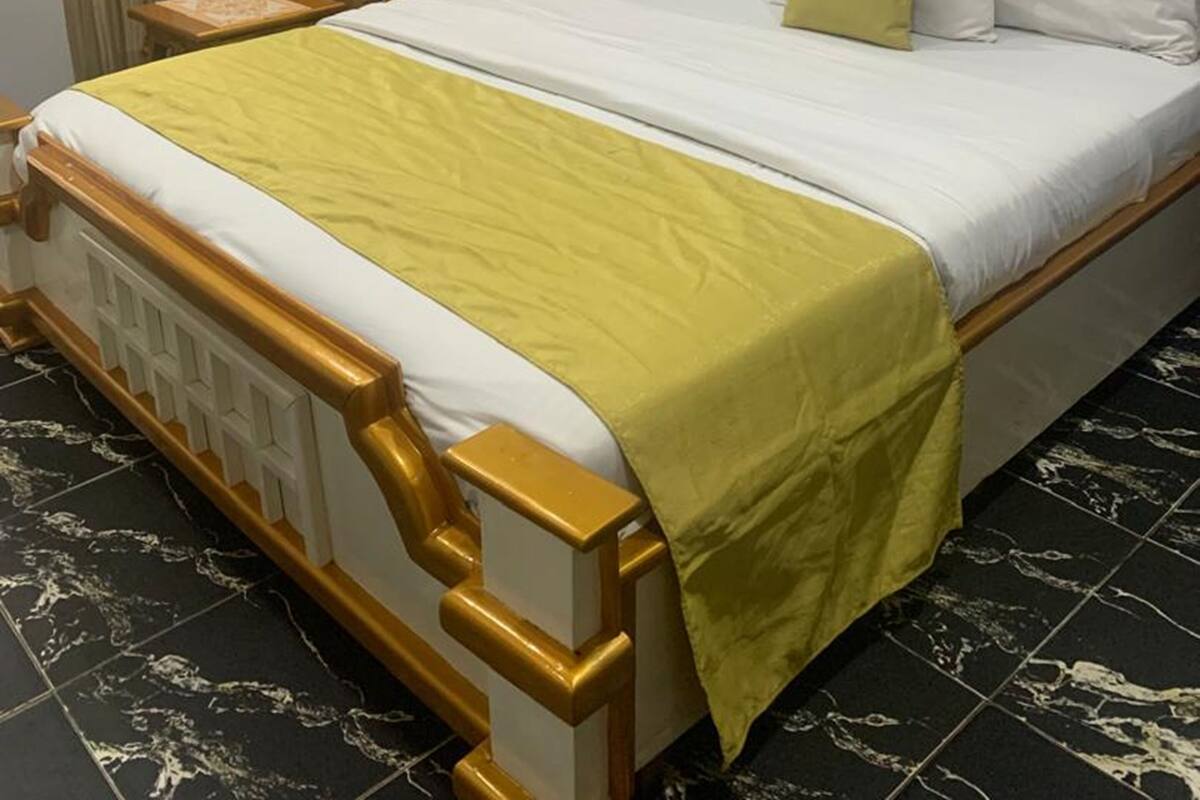 Une chambre d’hôtel avec un lit, un fauteuil doré, un climatiseur fixé au mur et un tableau encadré.