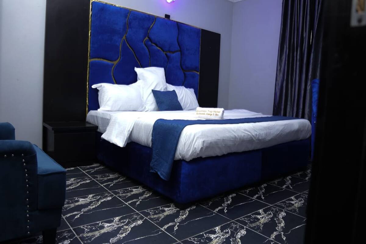 Une chambre d’hôtel moderne, dotée d’un grand lit, d’une tête de lit au design original et d’une enseigne indiquant le nom de l’hôtel.