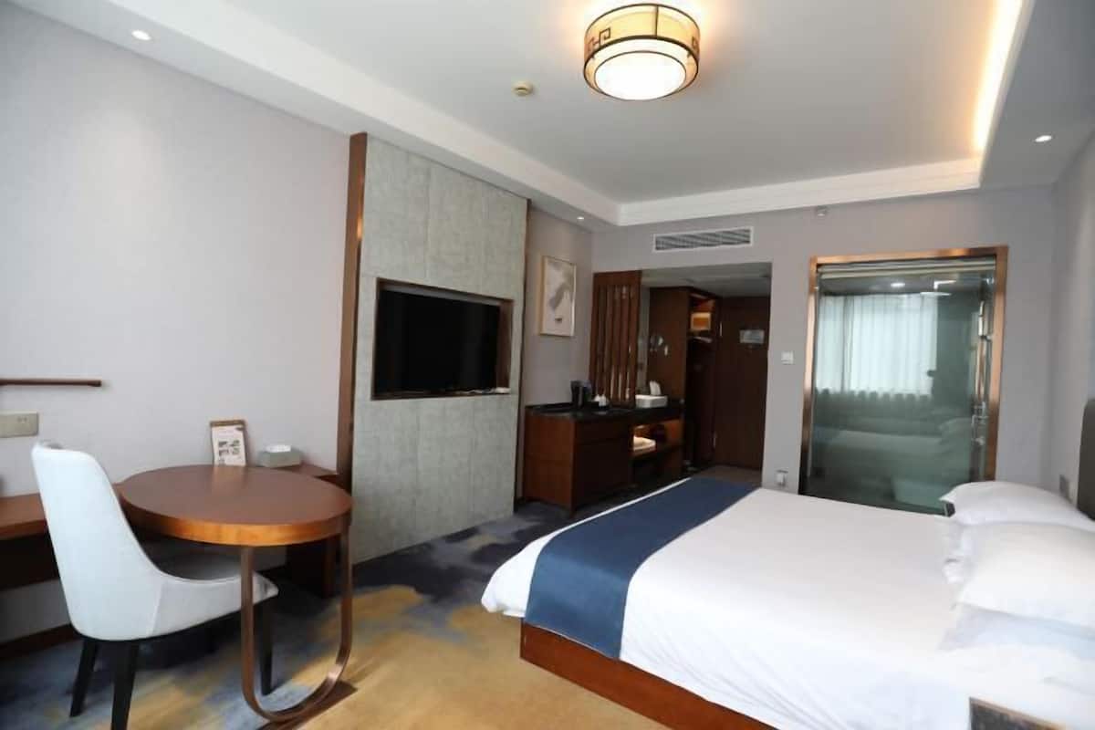 A hotel room with a bed, a desk, a chair, a TV, and a bathroom door.