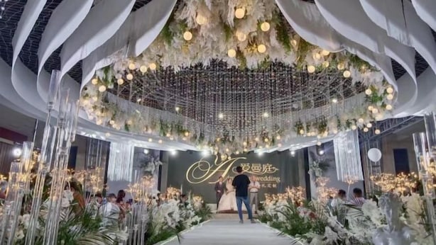 A wedding venue with a central aisle, floral decorations, and hanging lights. - Huaian Hotel (Huai'an)
