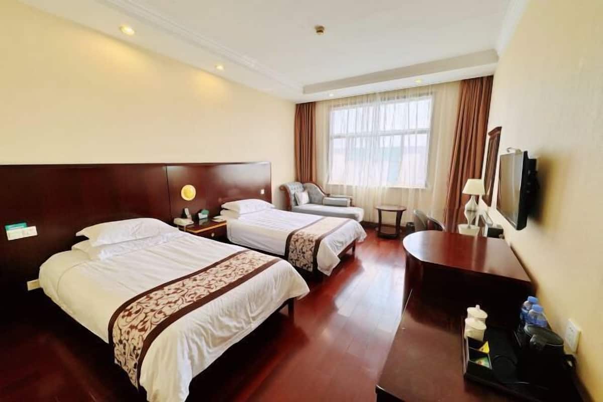 A hotel room with two beds, a desk, a chair, a TV, and a window with curtains.