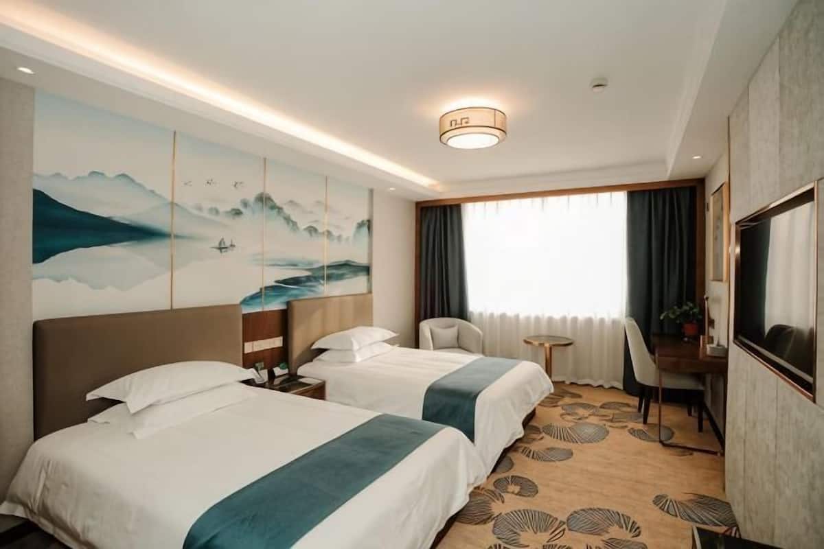 A hotel room with two beds, a desk, a chair, a TV, and a painting on the wall.