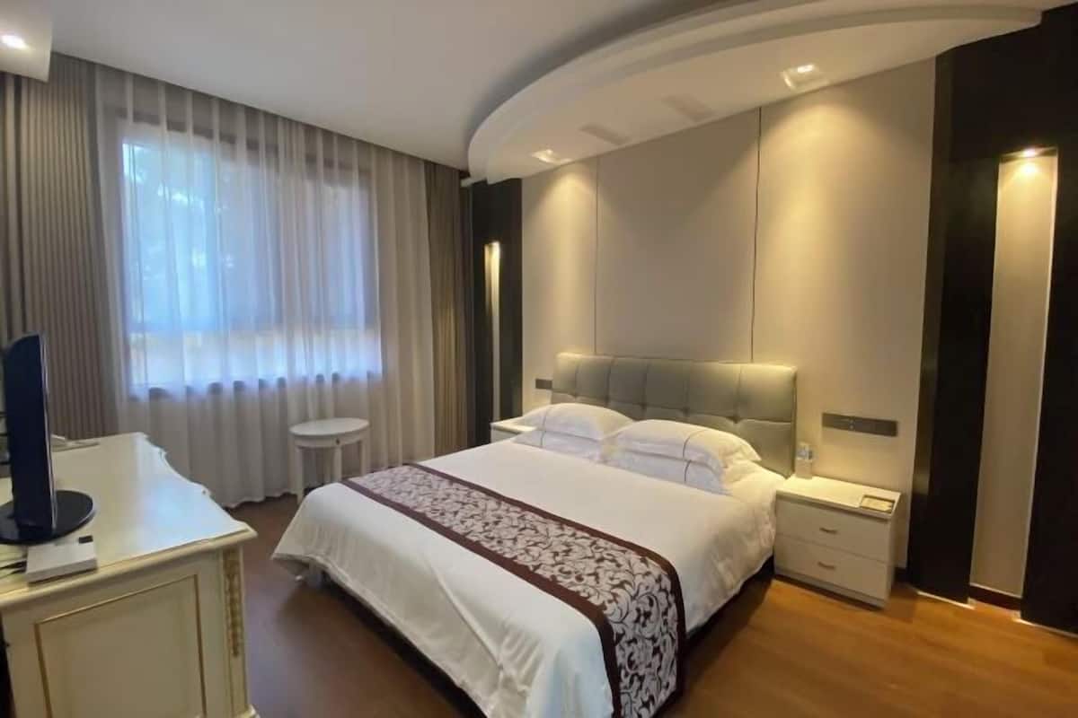 A modern hotel room with a large bed, a bedside table, a desk, and a chair.