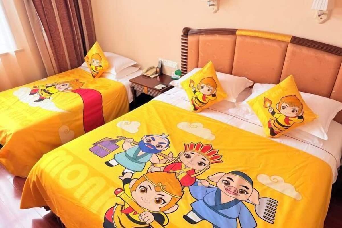 Two twin beds with matching yellow bedding and cartoon character prints, a wooden headboard, a bedside table with a lamp, and a wall-mounted light fixture.