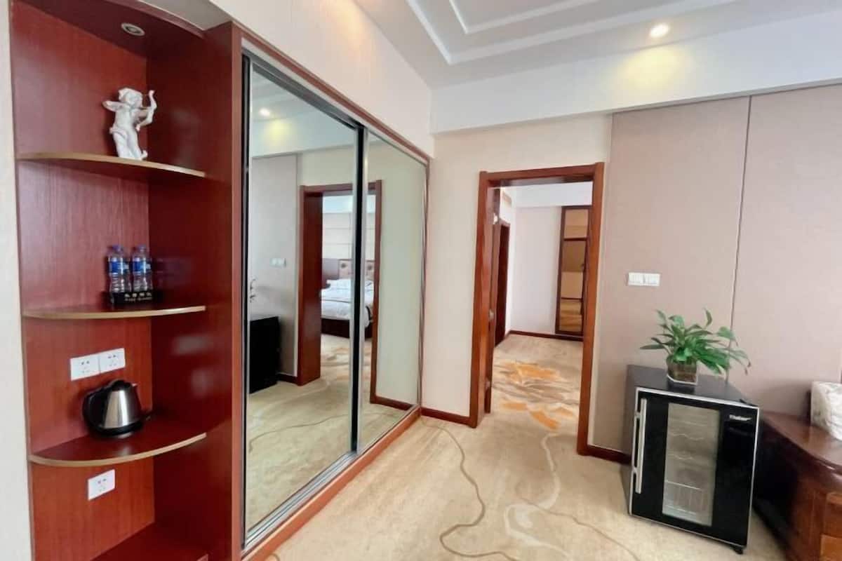 A hotel room with a sliding door, a small refrigerator, a shelf with a kettle, and a water dispenser.