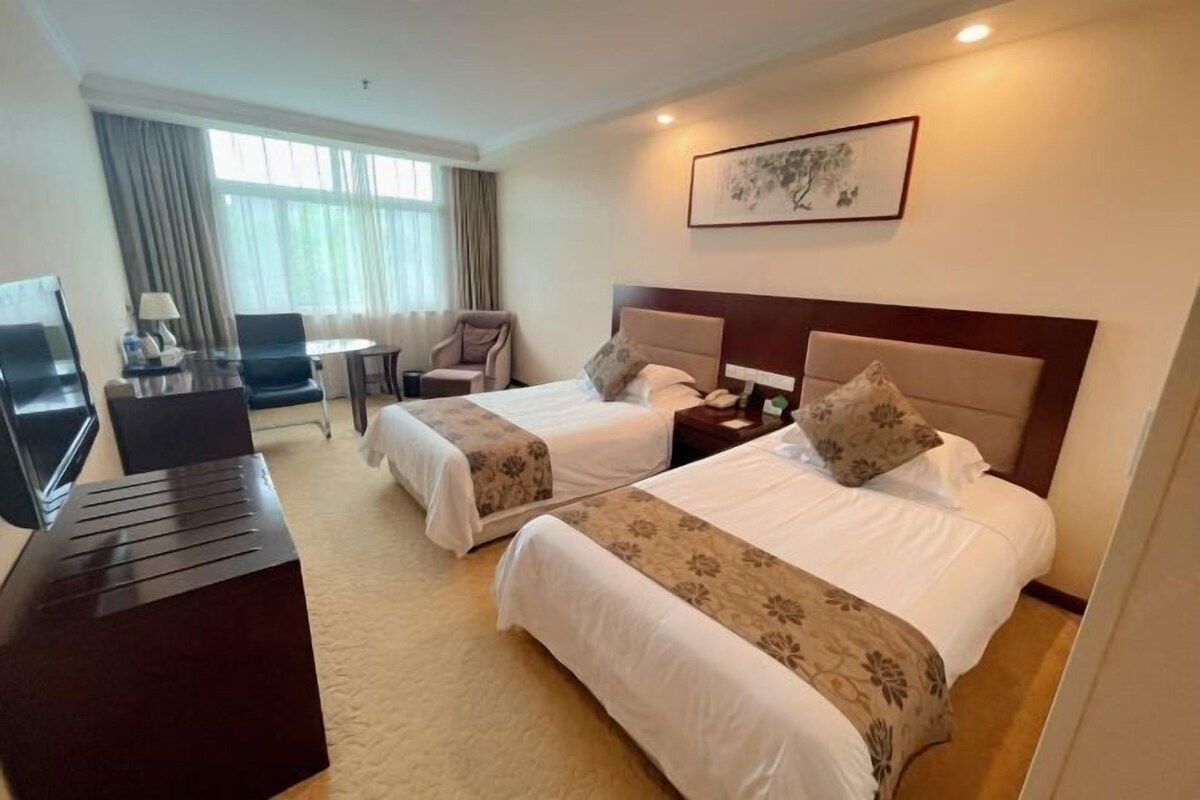 A hotel room with two beds, a desk, a chair, a TV, and a window with curtains.