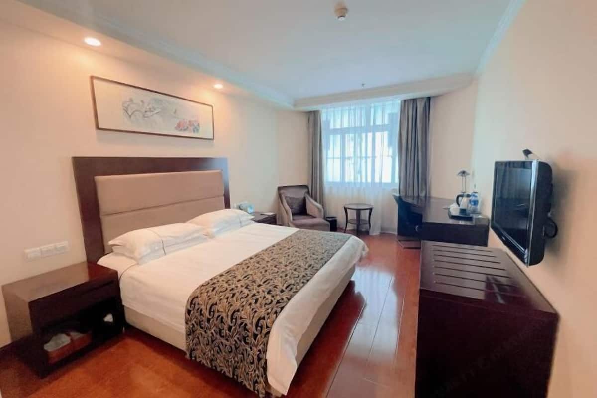 A hotel room with a large bed, a desk with a television, a chair, and a window with curtains.