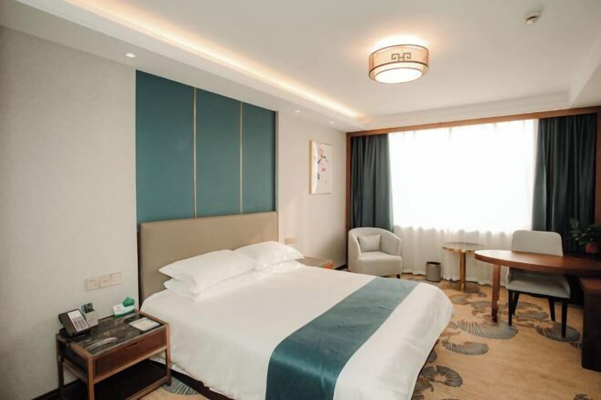 A hotel room with a bed, a desk, a chair, a small table, and a window with curtains.