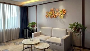 A modern living room with a sofa, two round tables, a decorative wall piece, and potted plants. - Huaian Hotel (Huai'an)