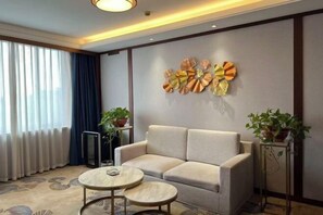 Een moderne woonkamer met een bank, twee ronde tafels, een decoratief wandobject en potplanten.