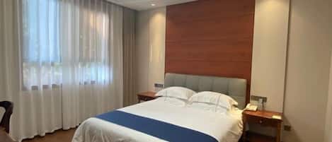 A hotel room with a bed, a nightstand, a desk, and a window with curtains.