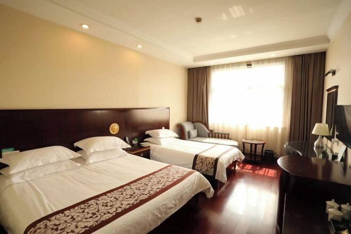 A hotel room with two beds, a desk, a chair, and a window with curtains.