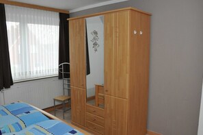 A bedroom with a wooden wardrobe, a bed with a blue and white striped bedspread, a window with sheer curtains, and a radiator.
