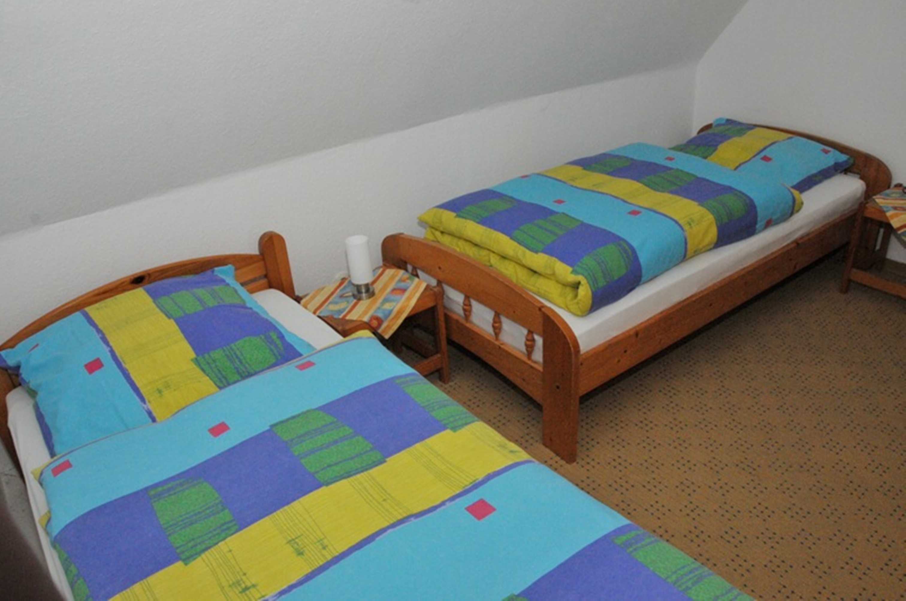 Een kleine kamer met twee houten bedden, elk voorzien van een kleurrijke sprei.
