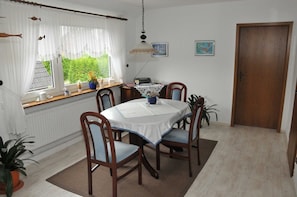 Ein Esszimmer mit einem runden Tisch, vier Holzstühlen, einer weißen Tischdecke und einem Fenster mit weißen Vorhängen.