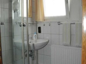 A bathroom with a glass shower enclosure, a white sink, and a towel rack.