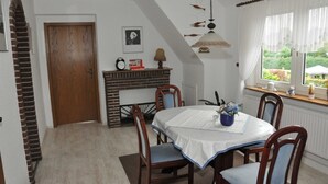 Uma sala de jantar com uma mesa redonda, cadeiras, lareira de tijolos e janela com vista para vegetação.