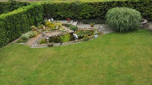Um jardim bem cuidado com um lago, diversas plantas e uma pequena construção.