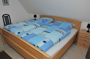 Ein Doppelbett mit einer blau-weißen Bettdecke, einem Holz-Kopfteil, einem Nachttisch mit Lampe und einer kleinen Kommode.