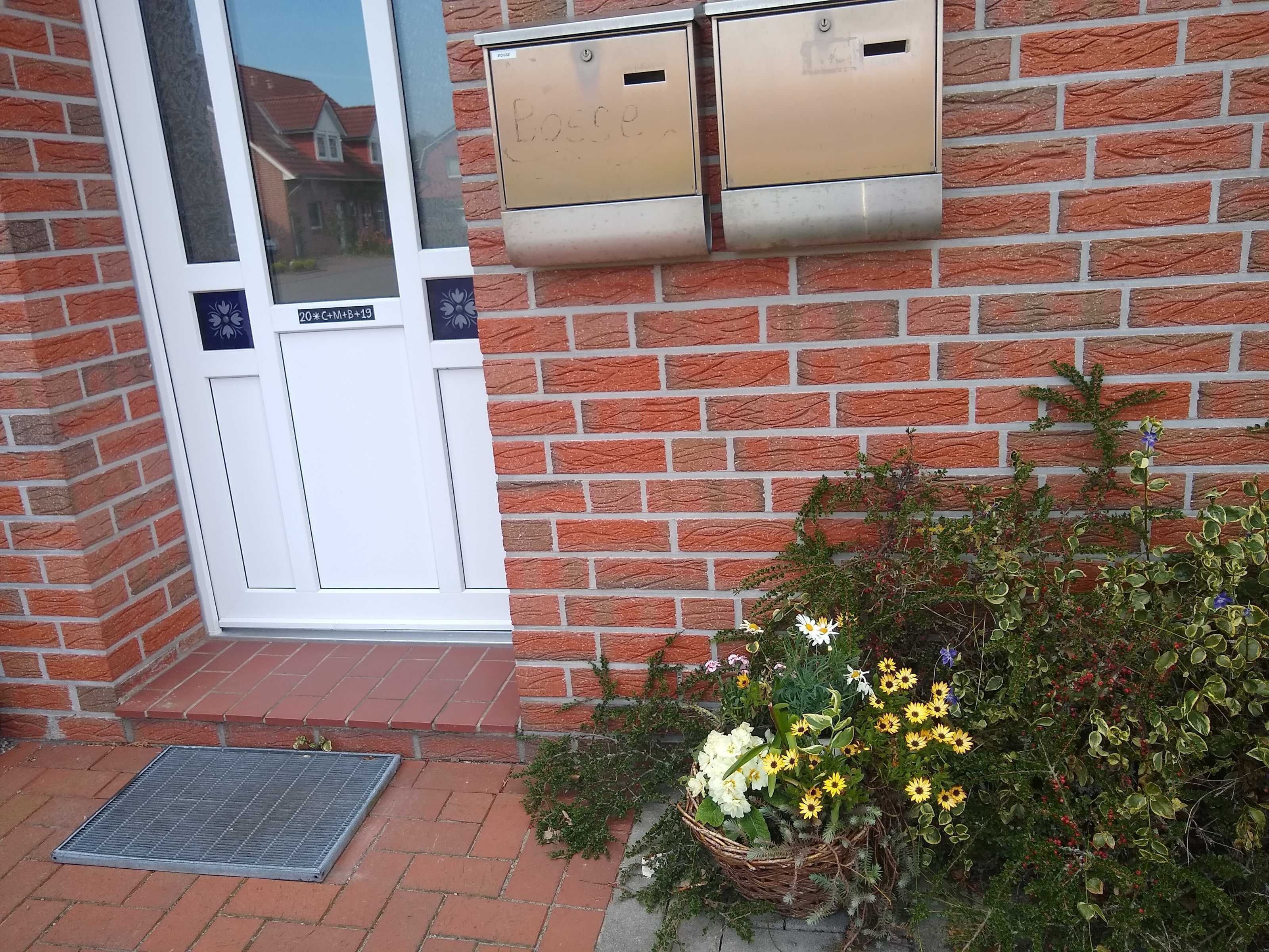 A brick building with a white door, two mailboxes, a small step leading to the door, and a metal grate on the ground.