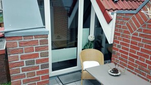 Pieni ulkotila, jossa on rottinkituoli ja pöytä, tiiliseinä sekä lasiovi, joka johtaa katettuun terassiin.