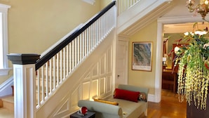 A staircase with white railings and a black handrail, leading to a room with a light blue sofa, a red pillow, and a small table with a red object. - The Inn On First (Napa)
