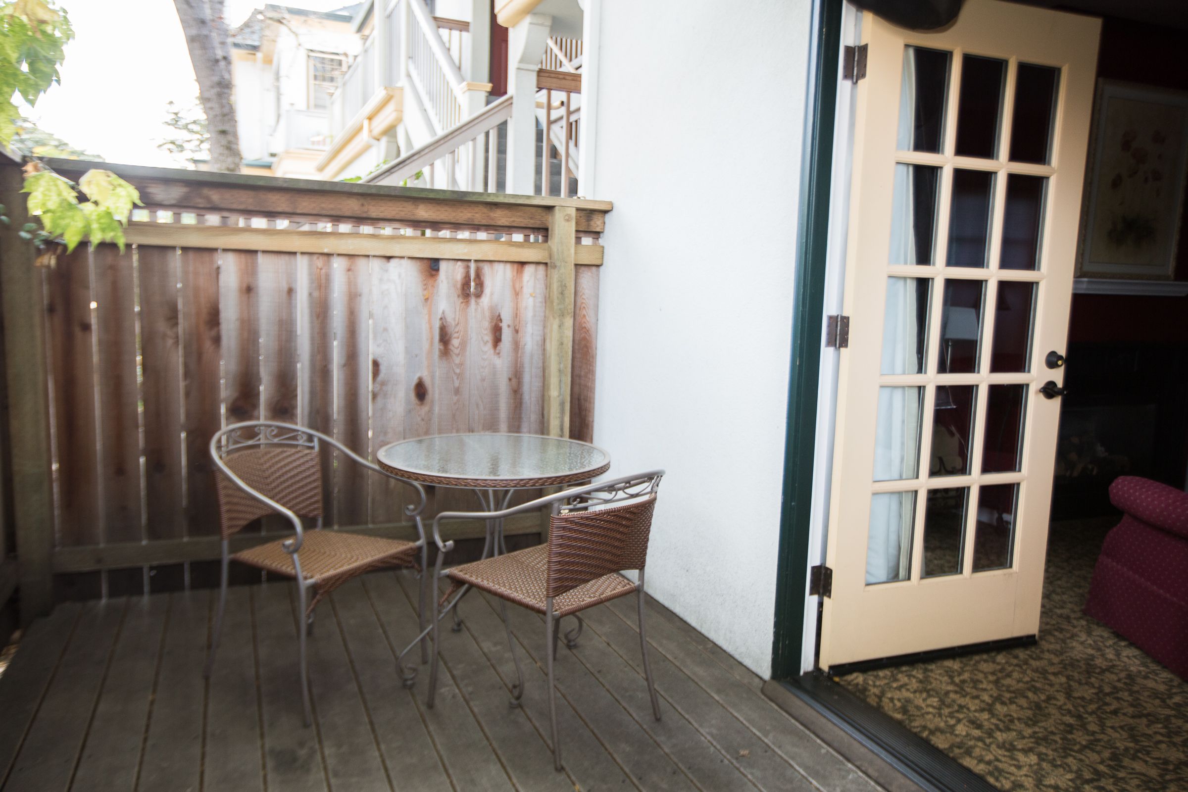 A patio with a table and two wicker chairs, a wooden fence, and a door leading to an interior room.