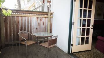 A patio with a table and two wicker chairs, a wooden fence, and a door leading to an interior room.