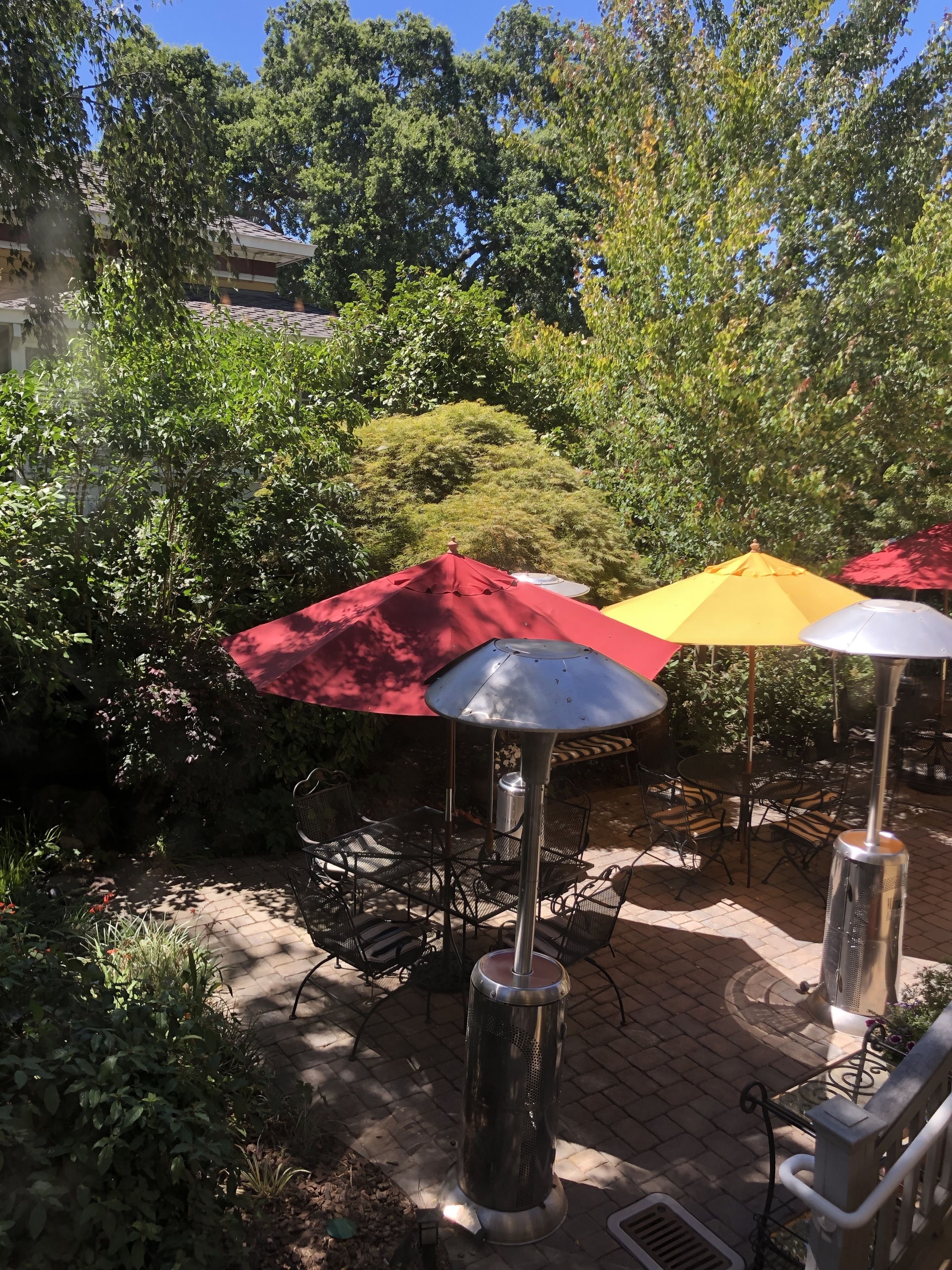 Espace extérieur aménagé avec des parasols et des chaises en métal, entouré de verdure et d’arbres.