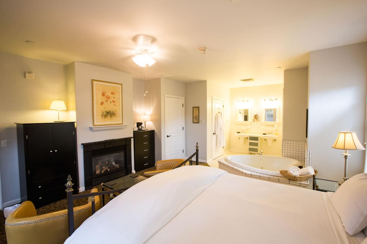 A hotel room with a large bed, a fireplace, a bathroom with a bathtub, and a mirror.