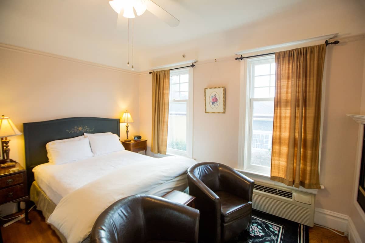 A hotel room with a large bed, two bedside tables, a chair, a window with curtains, and a radiator.