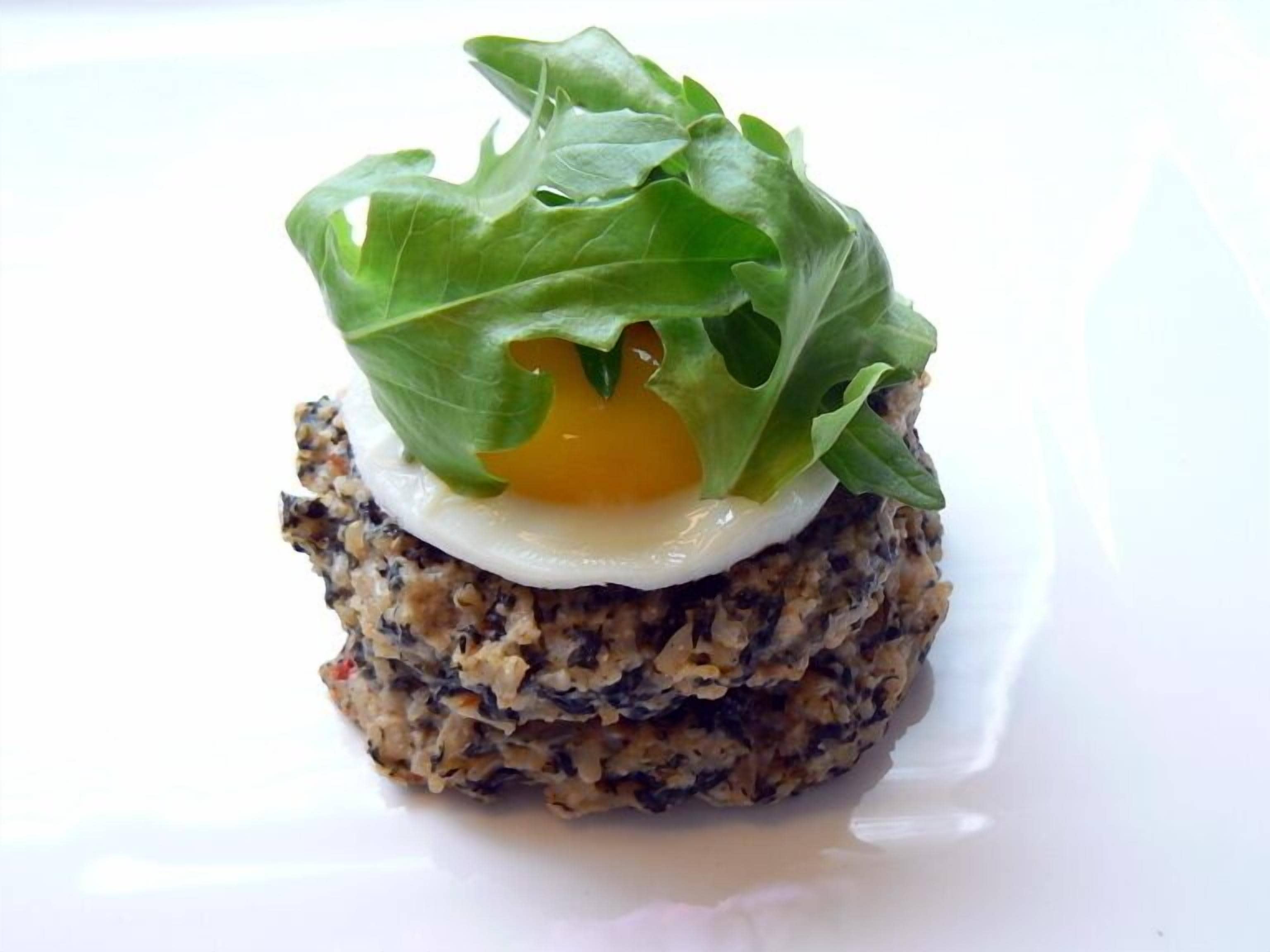 A dish with a poached egg on top of a grainy base, garnished with green leaves.