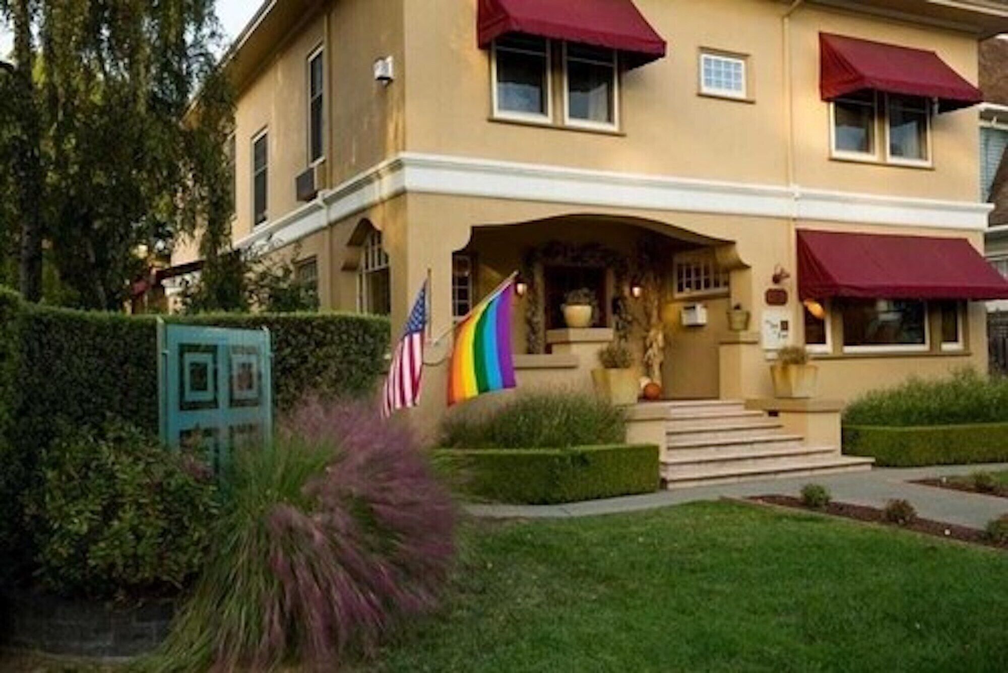 A two-story building with a symmetrical facade, a central entrance with steps, and a flagpole with a rainbow flag.