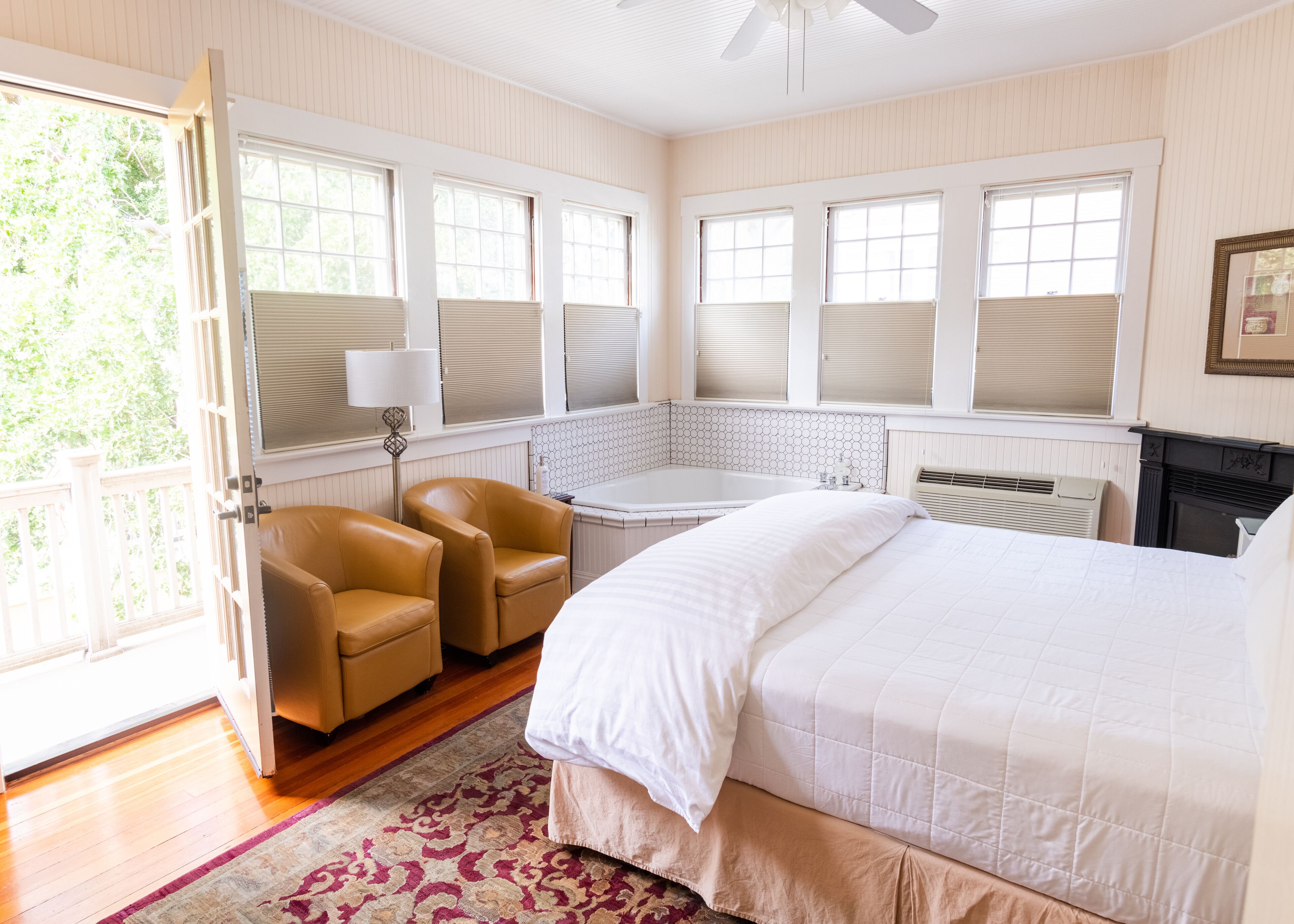 A bedroom with a large bed, a sitting area with chairs, a bathtub, and a view of the outdoors.