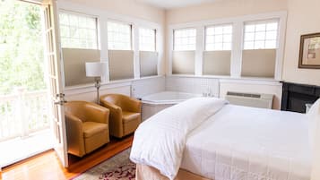 A bedroom with a large bed, a sitting area with chairs, a bathtub, and a view of the outdoors.
