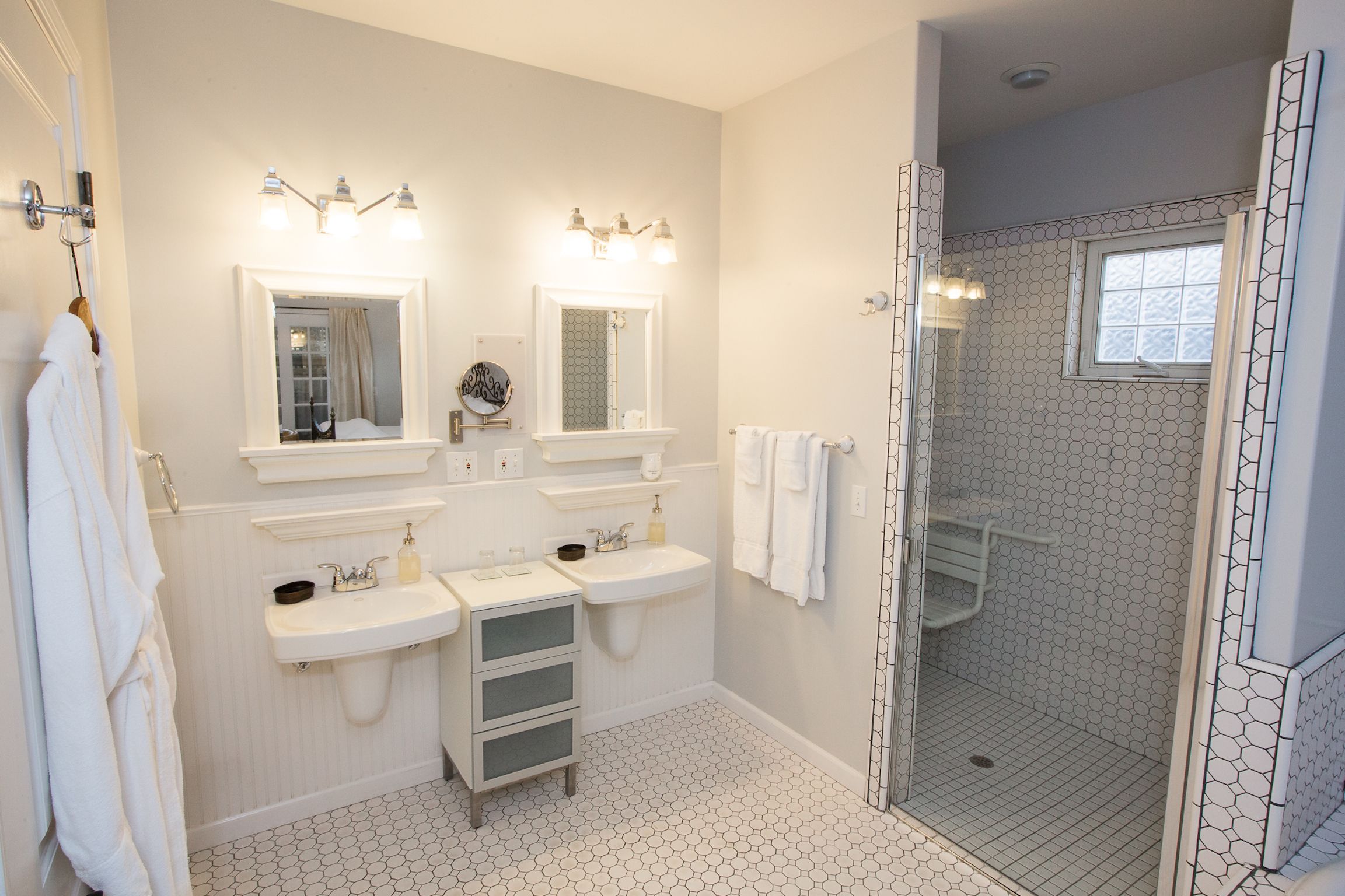 A bathroom with two sinks, a mirror, and a walk-in shower with a hexagonal tile pattern.