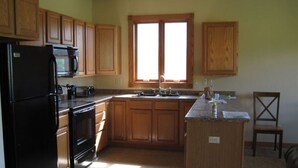 A kitchen with wooden cabinets, a black refrigerator, a stove, and a window with blinds.
