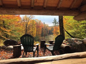Una cabaña de madera con dos sillas Adirondack mirando hacia un área boscosa con follaje otoñal.
