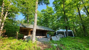 Une cabane rustique avec un toit en métal, entourée d’un feuillage verdoyant et dense et de gros rochers.