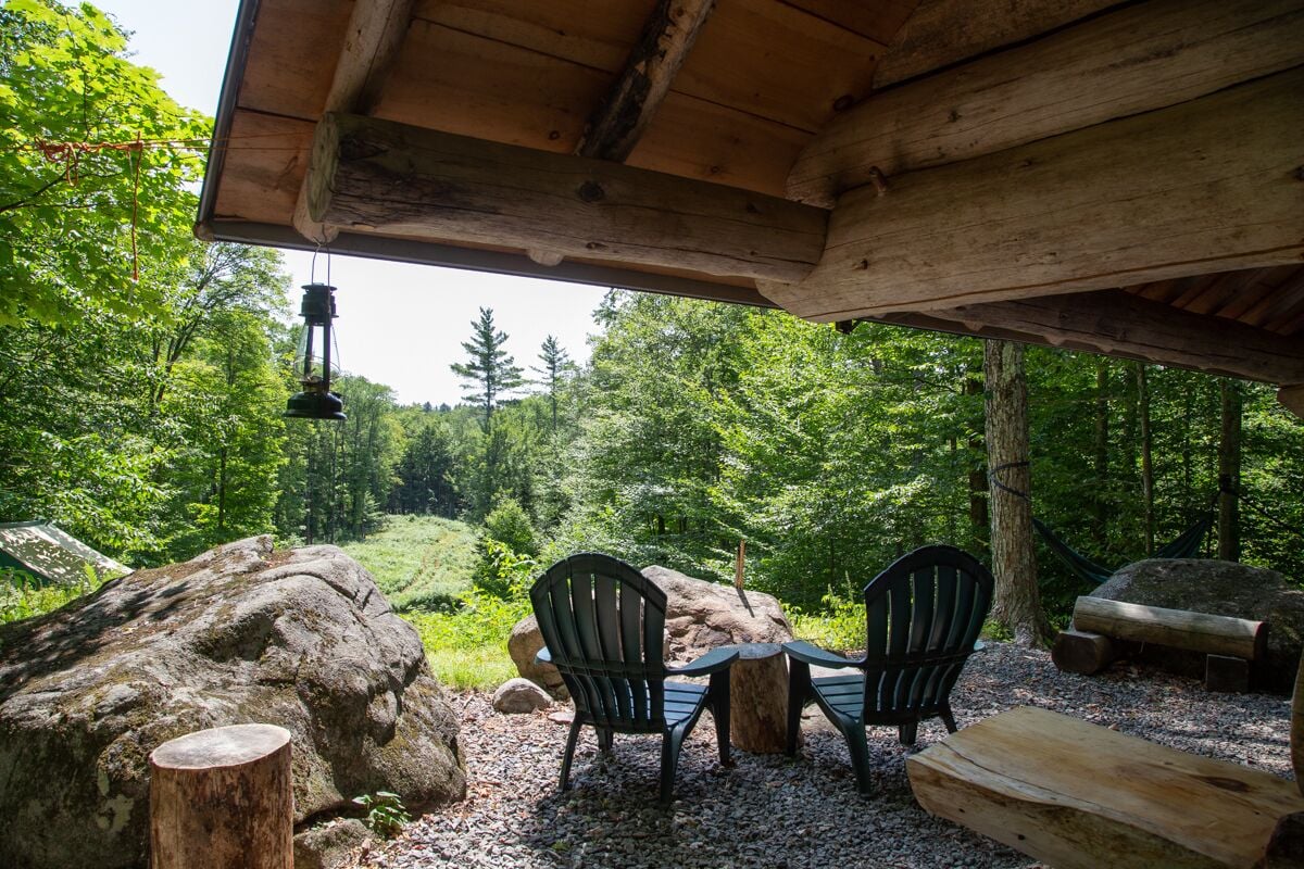 A rustic outdoor seating area with two chairs and a table, surrounded by natural scenery and wooden logs.