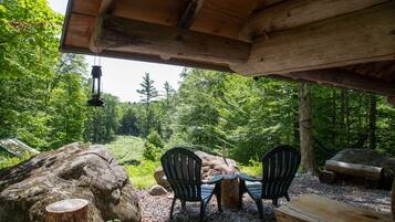 A rustic outdoor seating area with two chairs and a table, surrounded by natural scenery and wooden logs.