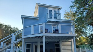 Ein zweistöckiges Haus mit überdachter Terrasse, die mit Gartenmöbeln und einer Treppe ausgestattet ist.