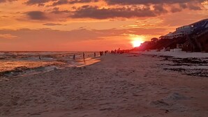 Ein Strand mit Sonnenuntergang, einer Promenade und Gebäuden entlang der Küste.