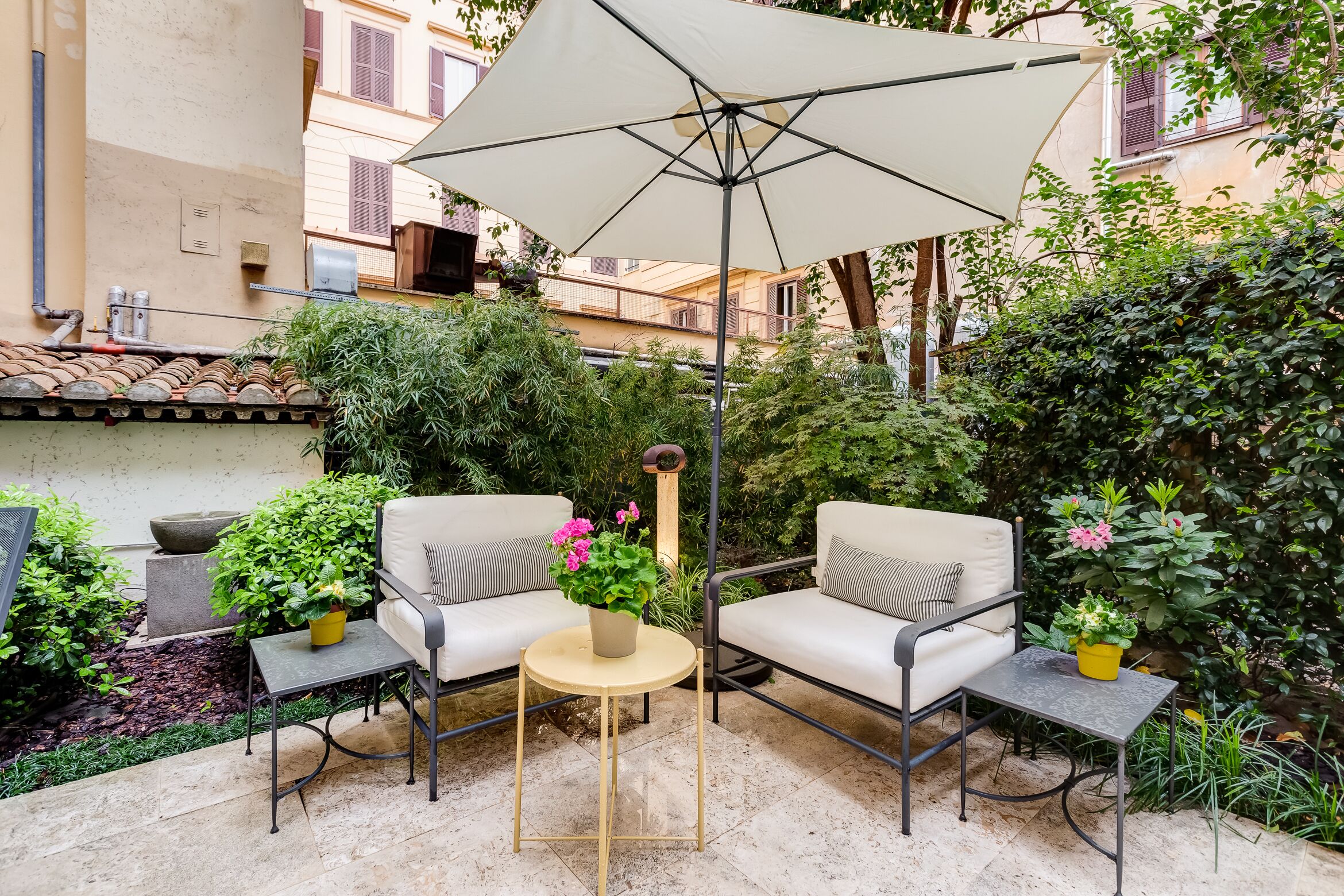 An outdoor seating area with two chairs and a table, surrounded by greenery and a large umbrella.