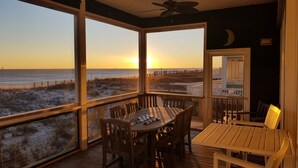 A covered outdoor seating area with a view of the beach and sunset.